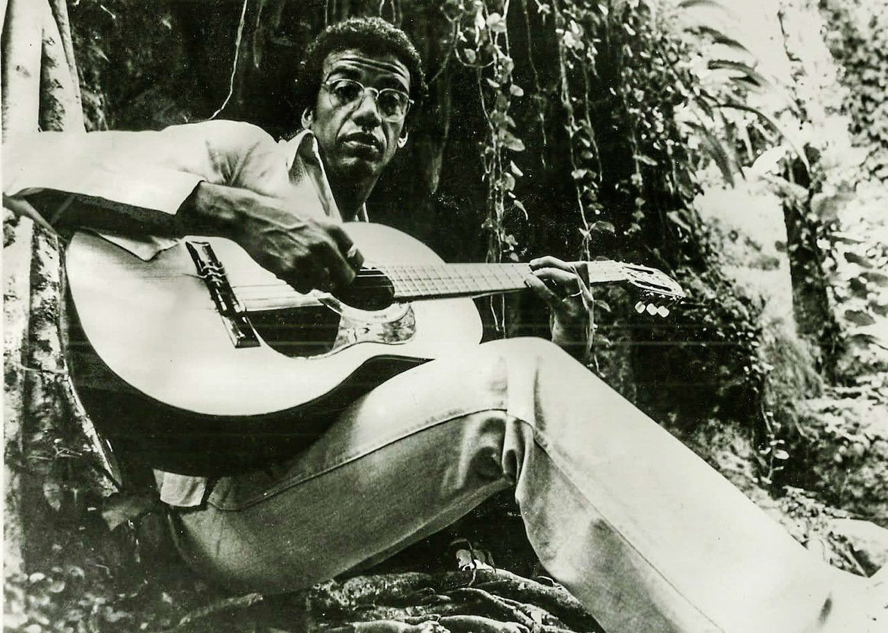 Black and white photo of Jorge Ben, leaning against a tree, guitar in hand